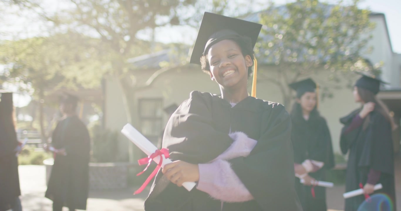 Ung afroamerikansk kvindelig dimittend smiler, hæver knyttet næve og krammer sit diplom efter ceremonien i studenterhue