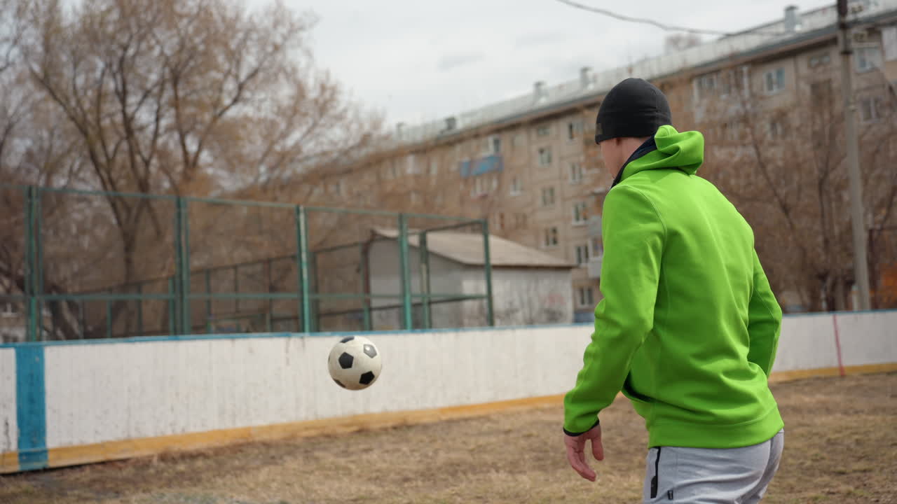 자신감 넘치는 길거리 운동선수가 축구공을 저글링하는 모습, 프리스타일 축구 기술을 선보이는 도시 공연가의 클로즈업, 축구공을 자신 있게 저글링하는 숙련된 개인을 포착한 생동감 넘치는 거리 풍경