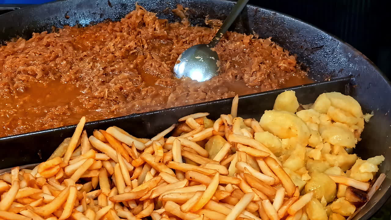 Hearty Latvian stew served with fried potatoes and crispy French fries in a large pan at a festive Midsummer food market in Latvia
