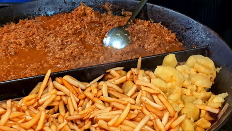 Hearty Latvian stew served with fried potatoes and crispy French fries in a large pan at a festive Midsummer food market in Latvia