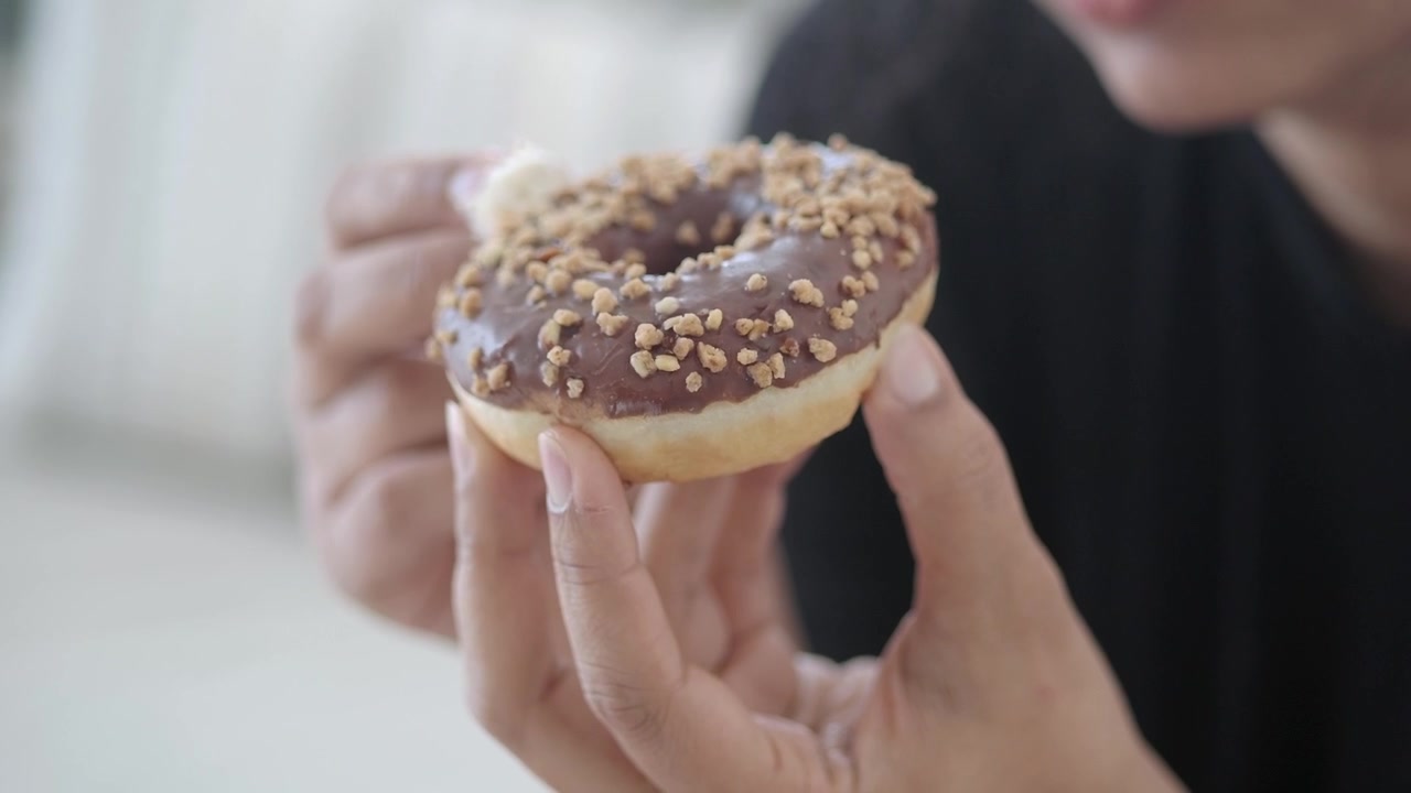 Persona che tiene in mano e mangia una ciambella glassata al cioccolato con granella