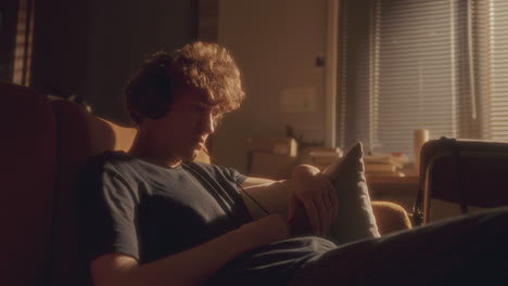 depressed man sitting on couch, listening to music with headphones