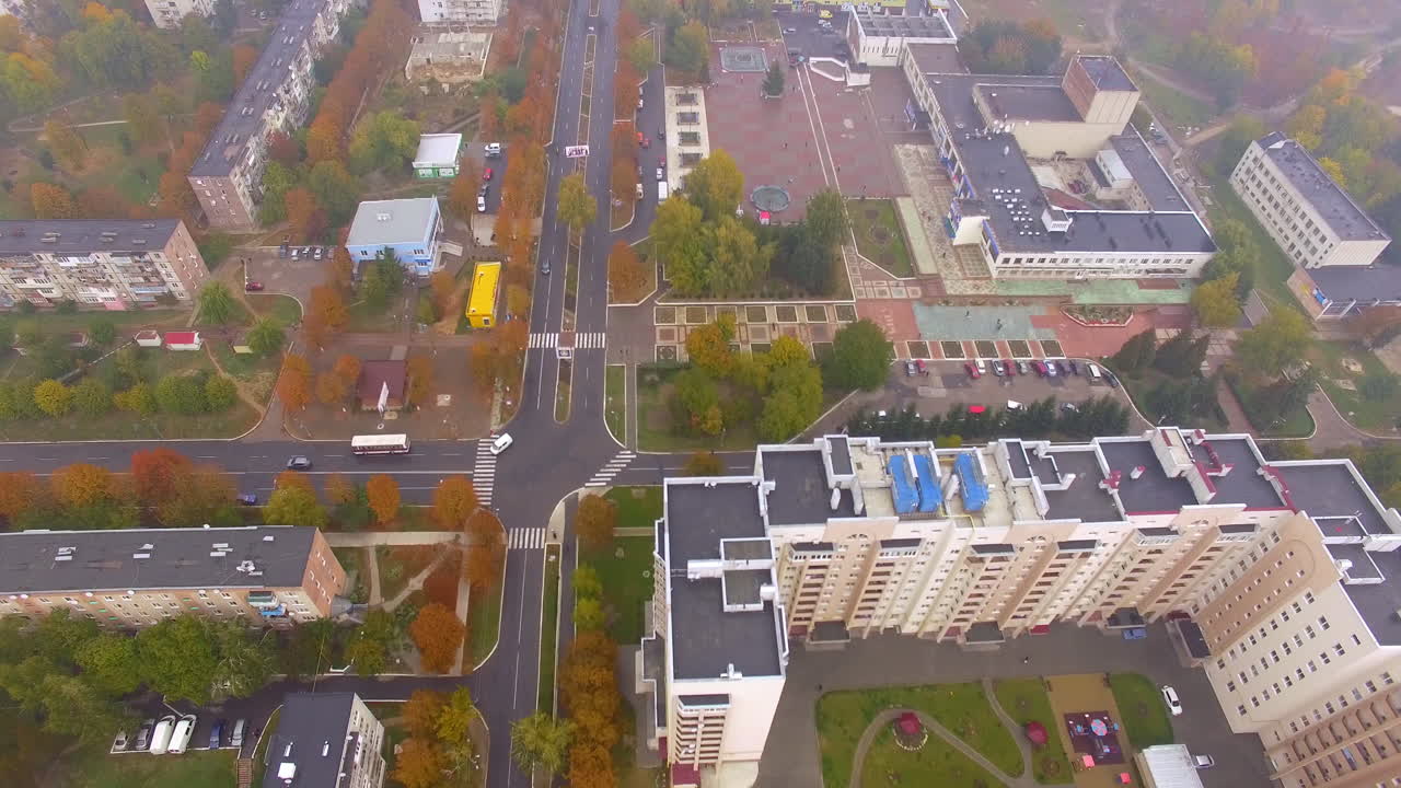 Bigger and smaller blocks of flats in the city downtown. Main roads with few cars passing by. Autumn foggy day backdrop.