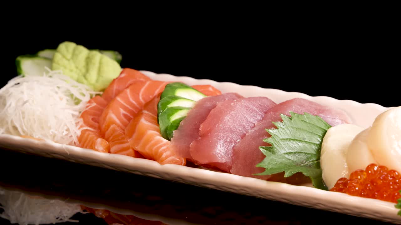 Chopsticks delicately pick up a slice of salmon sashimi from an assorted sushi platter under bright studio lighting, highlighting fresh seafood and vibrant garnishes