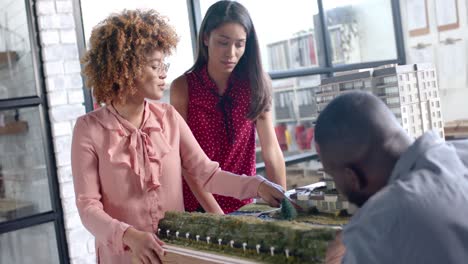 busy diverse colleagues discussing work over city model on table in office in slow motion