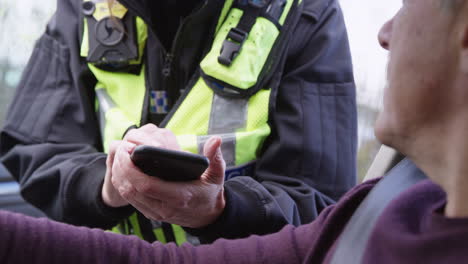 close up of male driver being stopped by female traffic police officer taking notes on mobile phone