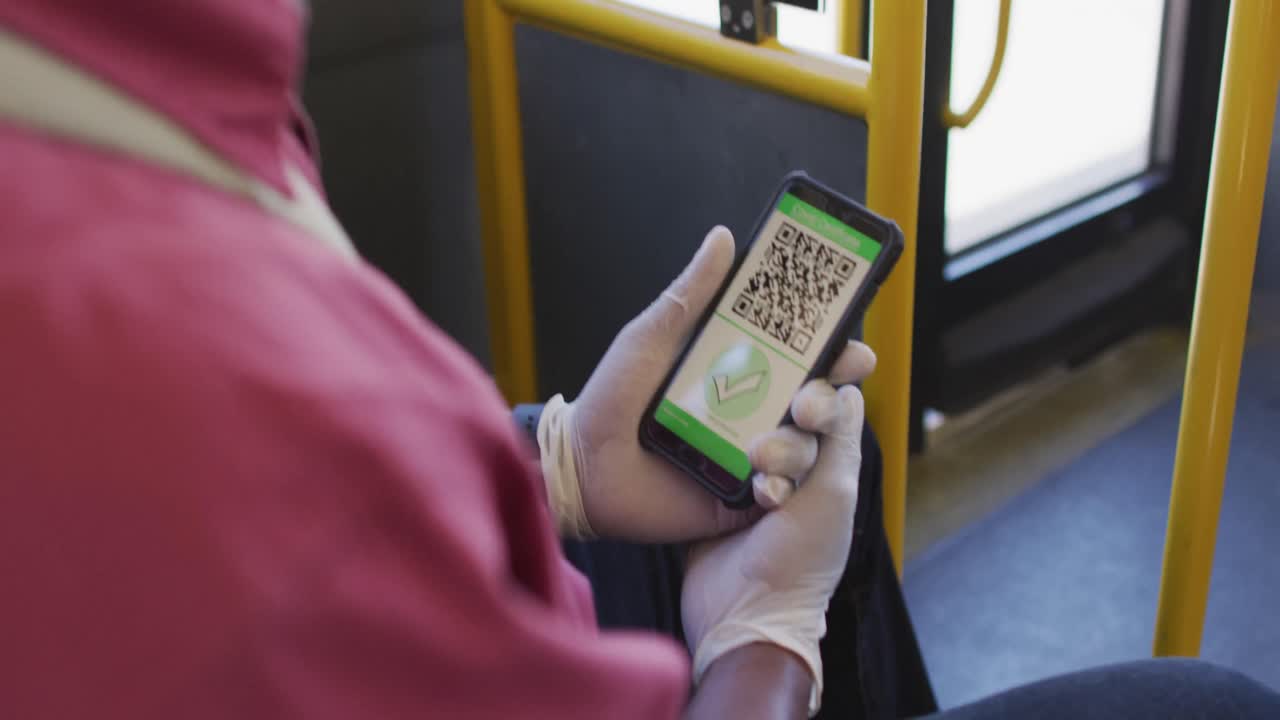 manos de un hombre afroamericano con guantes médicos, usando un teléfono inteligente con pasaporte covid en el autobús
