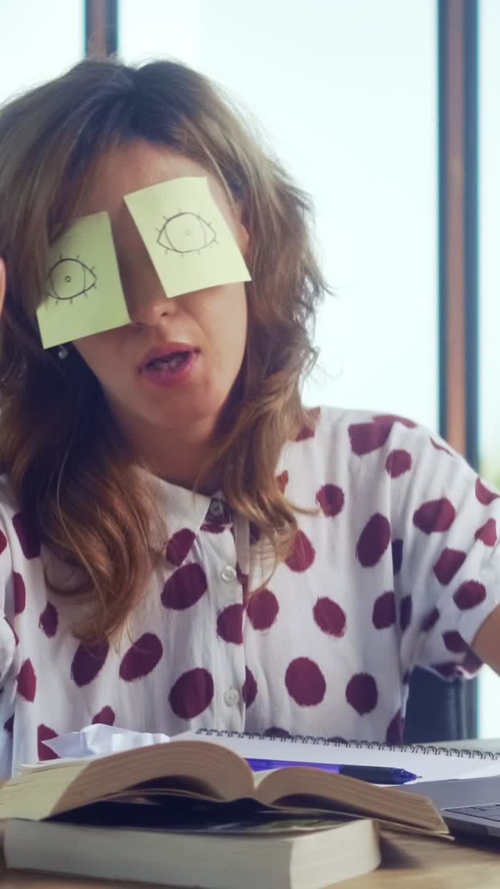 Woman engages in playful study break with sticky notes on eyes