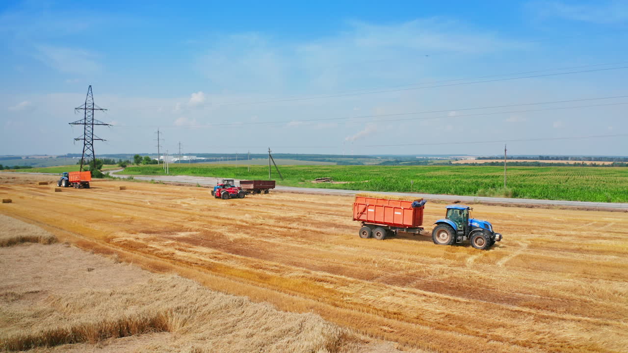 Agricultural machine moving by the cut wheat field. Tractor downloaded with hay bales rides by the plantation. High angle view.
