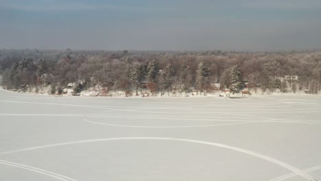 Aerial,-snow-covered-frozen-lake-with-snowmobile-vehicle-tracks-during-the-day