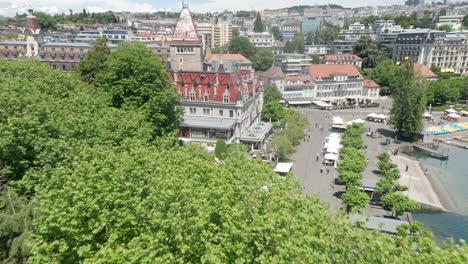 drohne fliegt über grüne bäume in richtung schöner hotelburg und neigt sich zu einem geschäftigen schwimmbad