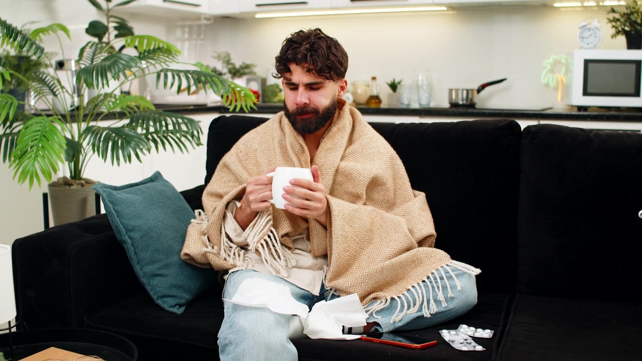Uomo indiano sotto una coperta che usa lo smartphone leggendo consigli medici e suggerimenti per la salute mentre si sente male.