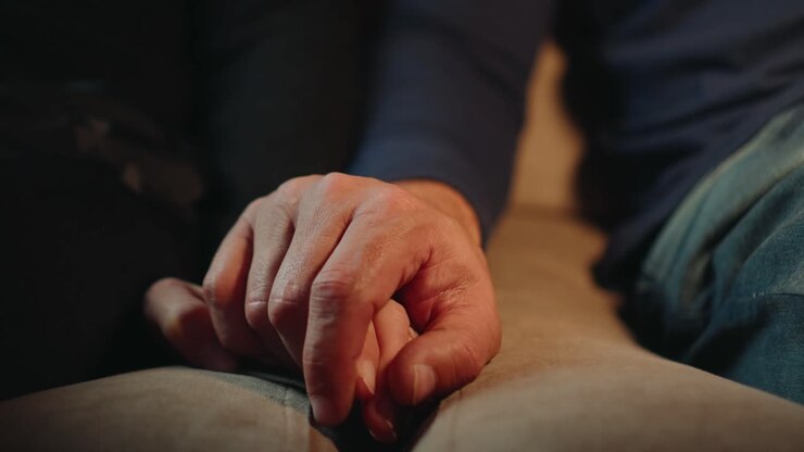 Closeup of the hands of a man and a woman holding each other while sitting on a sofa watching tv