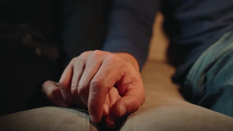 Closeup-of-the-hands-of-a-man-and-a-woman-holding-each-other-while-sitting-on-a-sofa-watching-tv