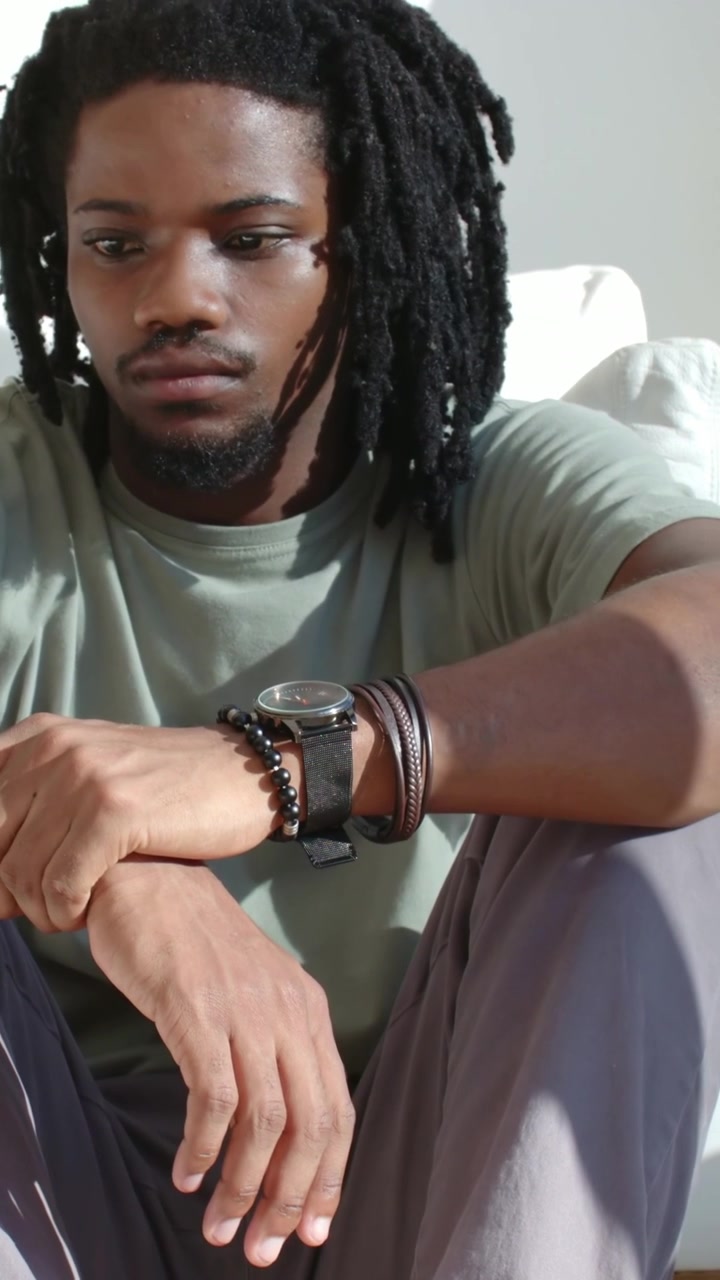 Vertical video: Panning up, showing man in green tee at home shifting gaze toward edge, with watch