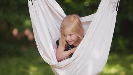 a little girl swings in the hammock in the garden holding a gift bag in the hands