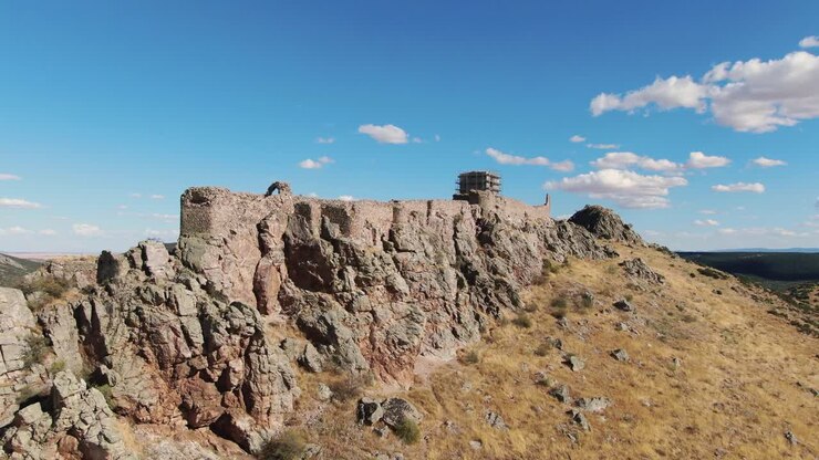 Un volo orbitale con drone rivela la disposizione allungata del Castello di Peñas Negras, costruito lungo una cresta rocciosa, mostrando come la fortezza si adatta allo stretto paesaggio collinare