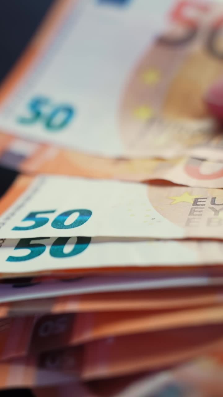 Vertikalt makro-nærbillede af en hånd, der tæller 50 euro-pengesedler på et mørkt bord med blød bokeh og bevægelsessløring – ideelt til koncepter om betaling, budgettering, bankvirksomhed eller svindel.