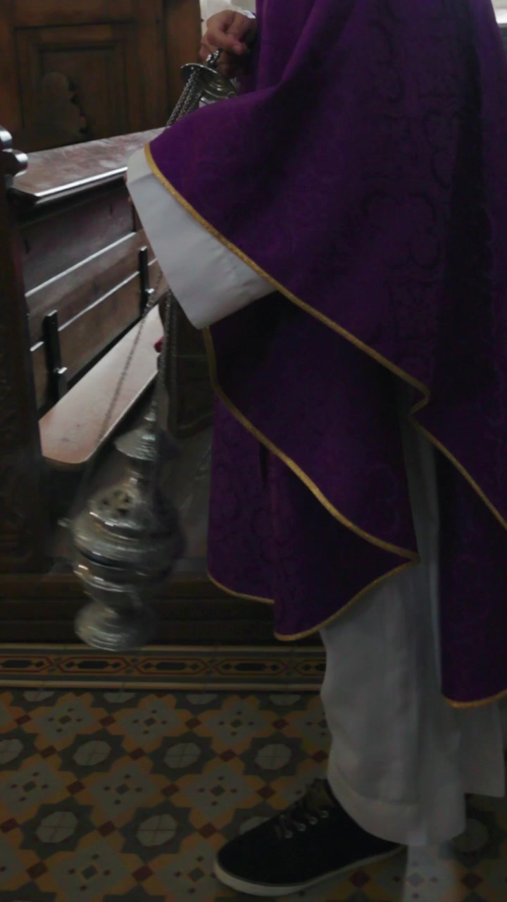 Sacerdote cattolico che porta e agita un turibolo di incenso mentre cammina lungo la navata nella
