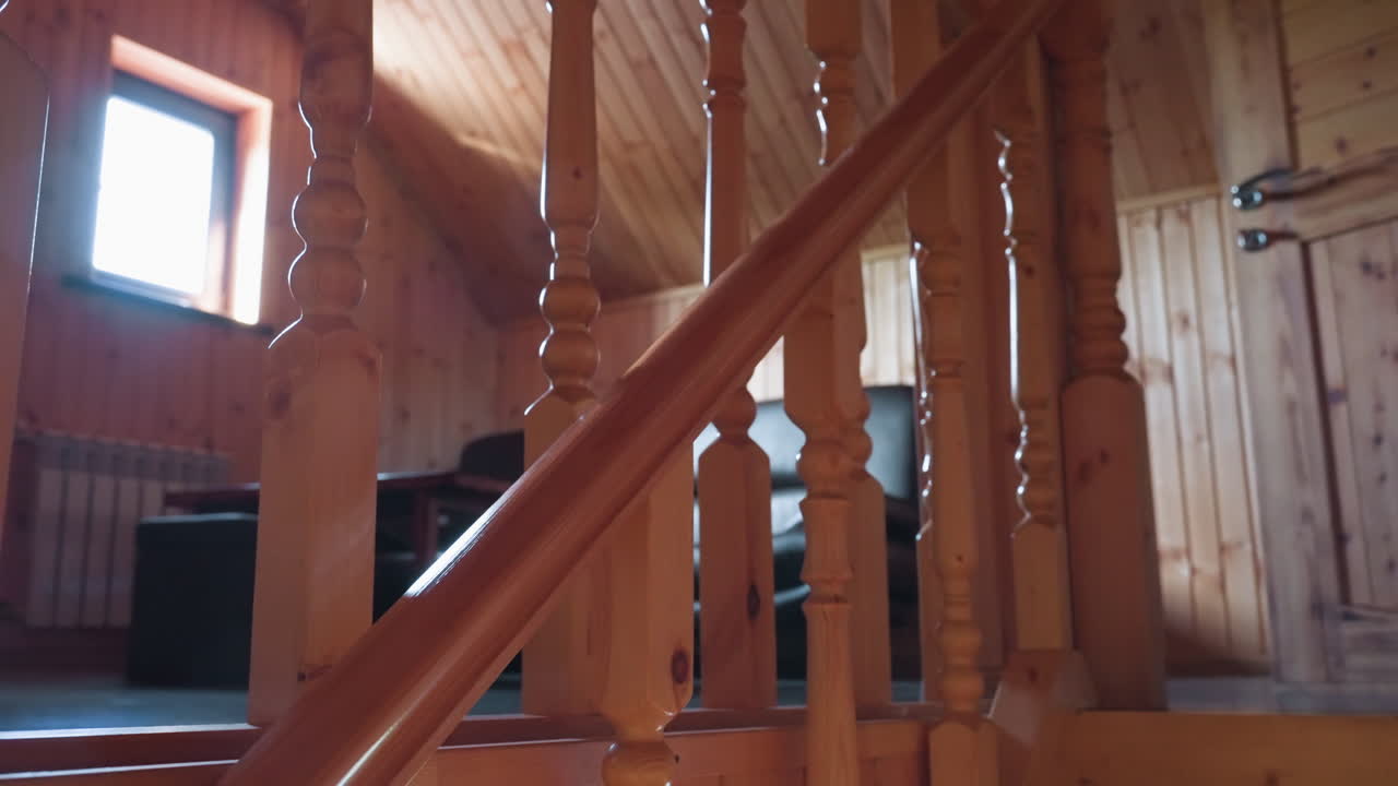 Warm toned wooden staircase with glossy carved railings and vertical wall paneling leads upward to rustic wood door with soft shadows and faint view of leather chair above