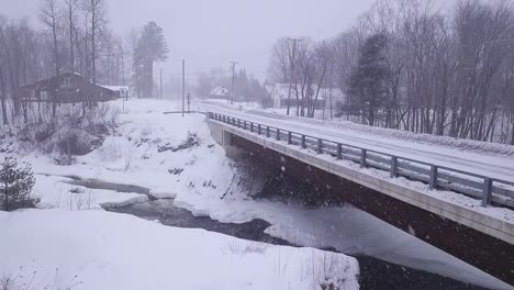 Luftaufnahme-In-Zeitlupe,-Die-Sich-Während-Eines-Schneesturms-Einer-Brücke-Nähert,-Die-Einen-Eisigen-Fluss-überquert