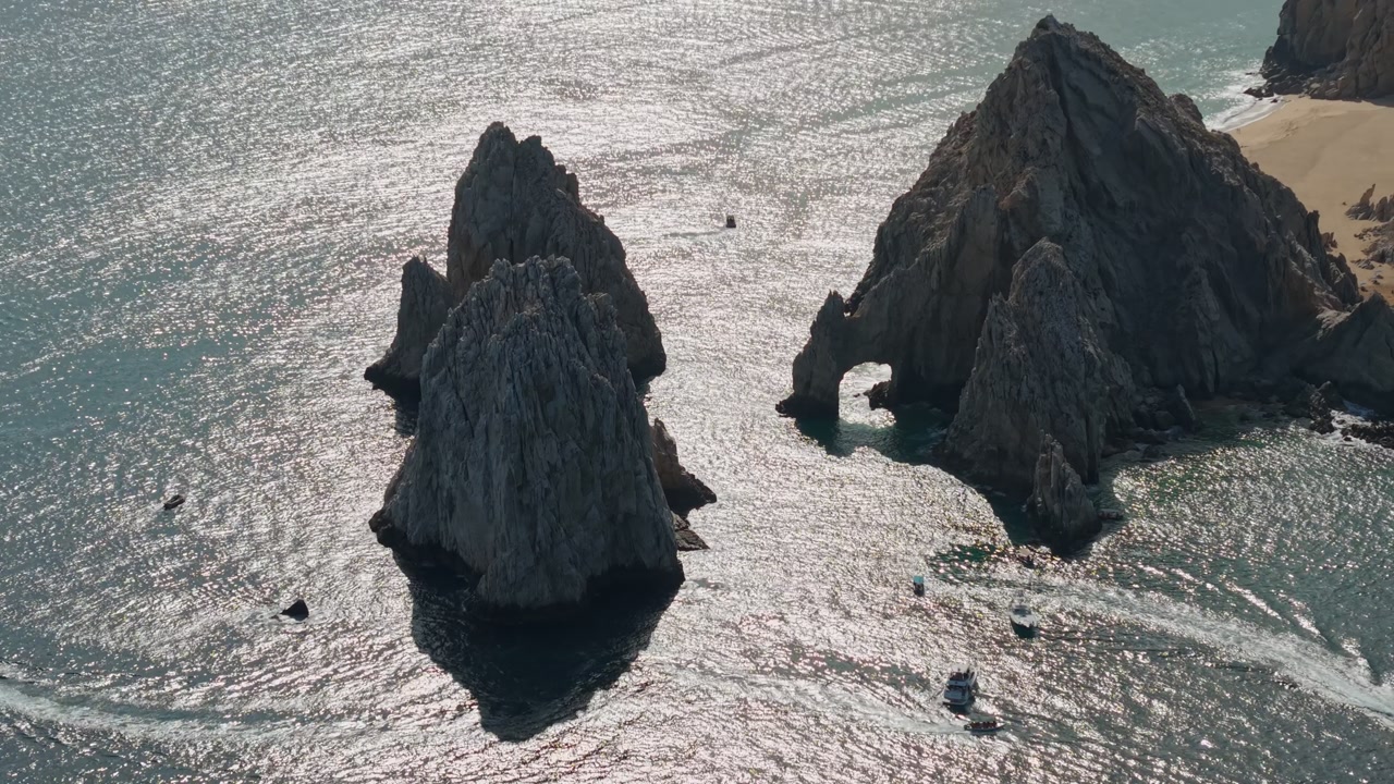 Aerial view of rock formations along the shores of Cabo San Lucas, the rock arch at Cabo San Lucas, and a sunny day reflected on the Sea of Cortez, Mexico