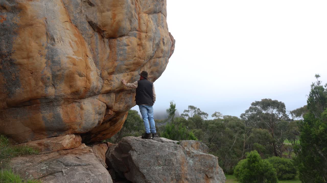 A bushman looks out accross the Australian outback while standing among big craggy rocky cliffs
