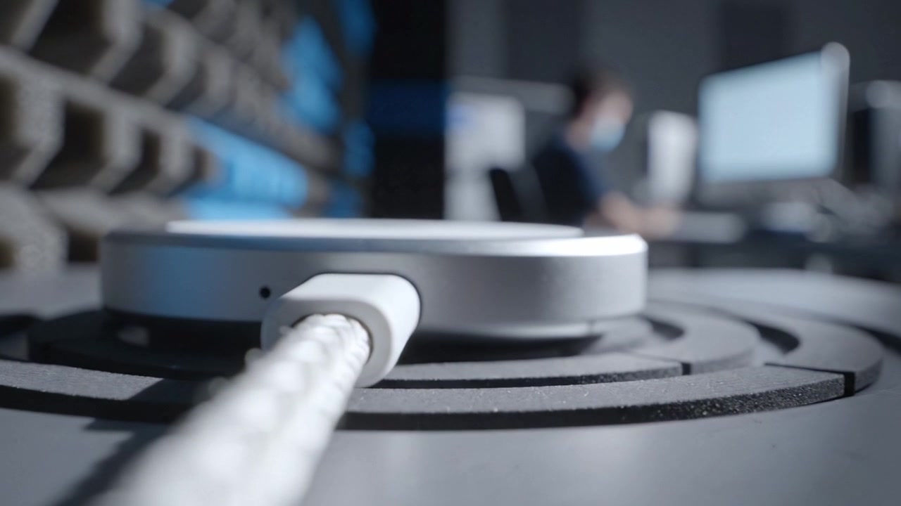 Close-up View of a Cable Connected to a Modern Device on a Desk, with an Out-of-Focus Background Showcasing a Busy Workspace Setting.