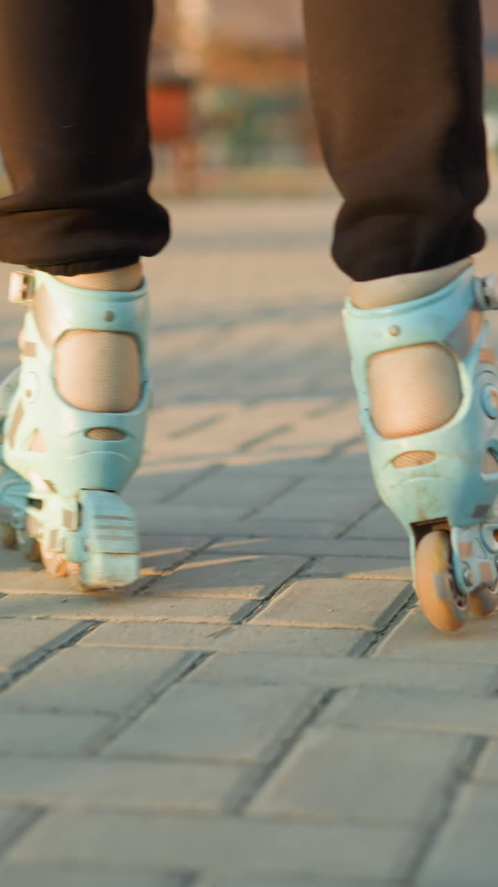 Close-up back shot of a person s feet wearing rollerblades, gliding smoothly along a paved path in a park during sunset. The golden light enhances the scene, highlighting the atmosphere of a park