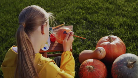 Back-view:-A-child-paints-a-pumpkin,-prepares-decorations-for-Halloween.-Sits-on-the-lawn-in-the-backyard-of-the-house