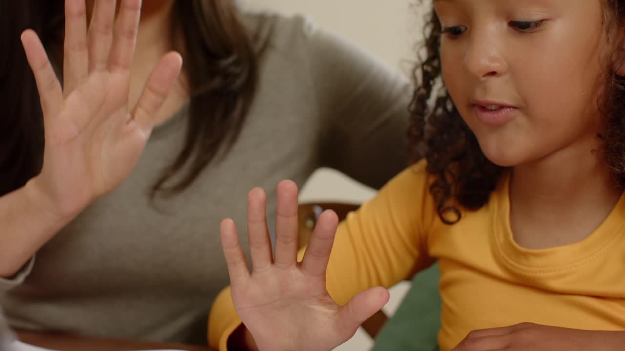 Mother and daughter counting with raising and mirroring numbers 2 to 5 on notebook at home