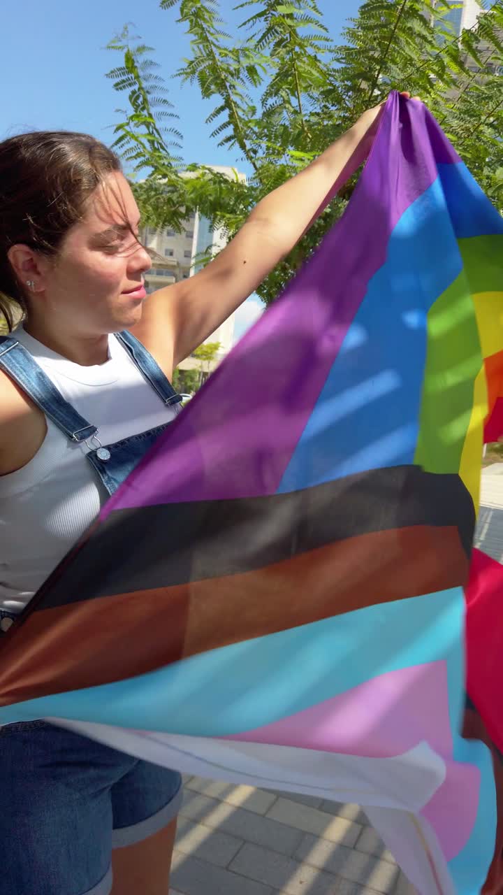 Young woman holding progress pride flag in the wind