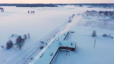 rural farm building with smoking chimney on cold winter day, aerial drone view