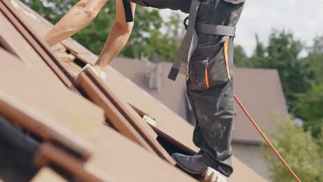 Hombre-Trabajando-En-El-Techo-Con-Cuerda-De-Seguridad,-Quitando-Clavos-De-Las-Tejas