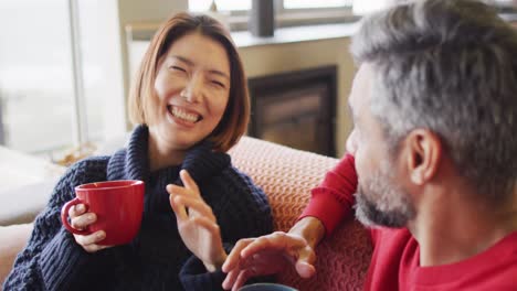 happy diverse couple sitting in living room drinking coffee and talking