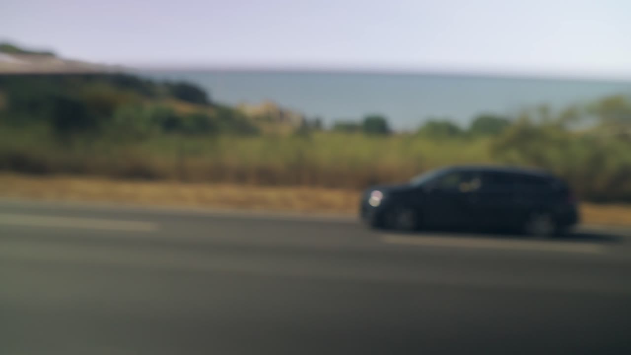 Blurred view from a moving vehicle on a sunny day, showcasing passing cars, roads, and distant landscapes