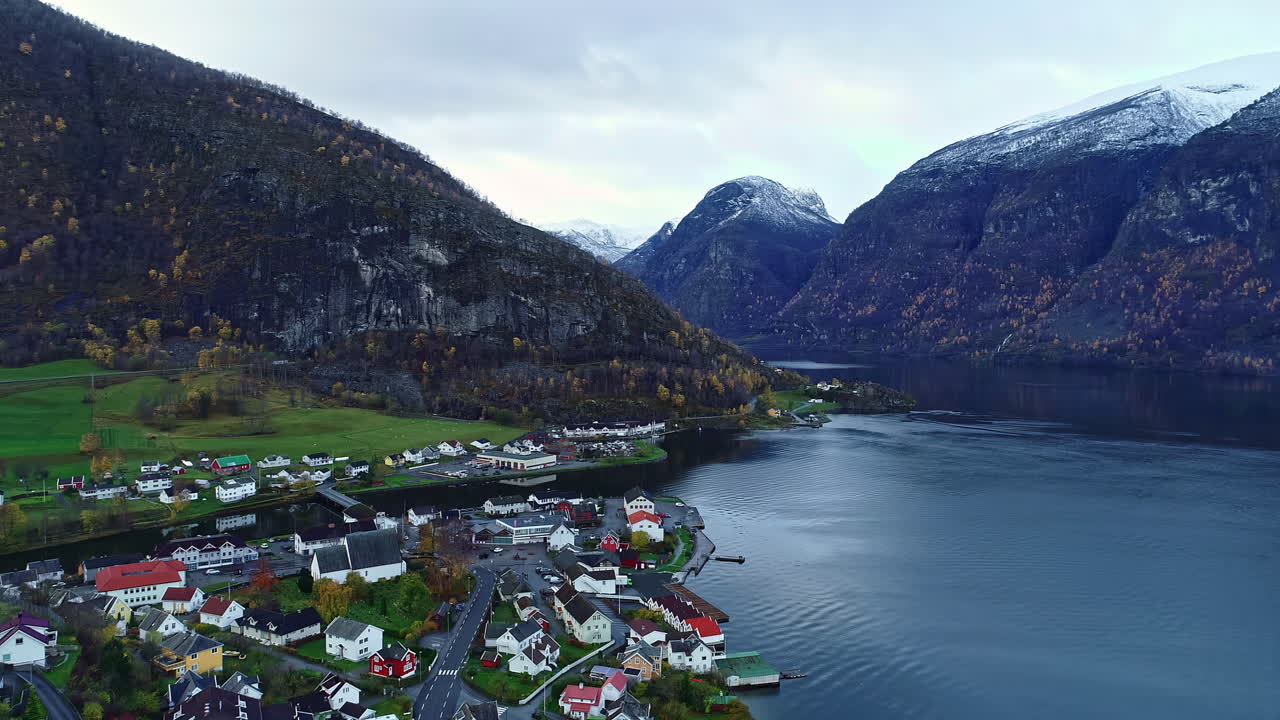vuelo de avión no tripulado en ascenso sobre un pueblo junto al lago en un valle rodeado de montañas cubiertas de nieve