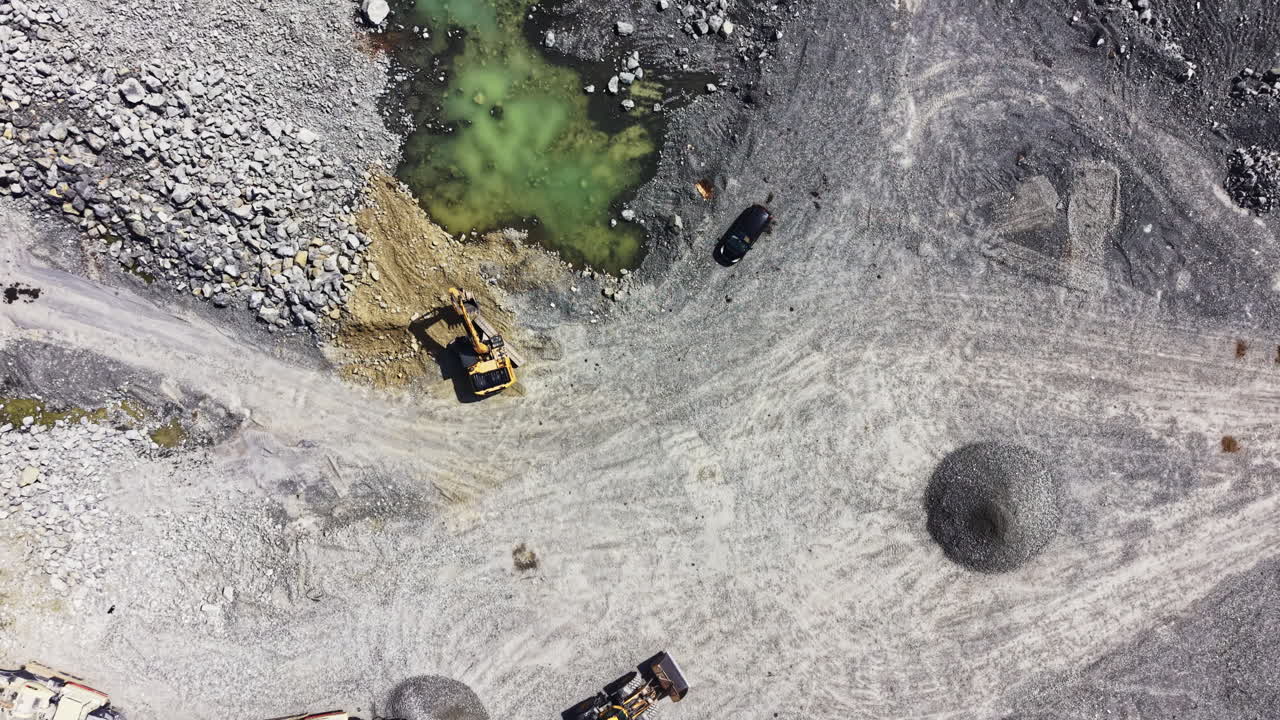 Granite quarry with heavy machinery working on site and water bodies nearby at midday