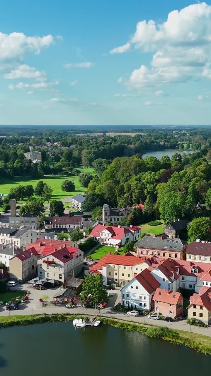Vertical aerial establishing shot captures the tranquil town of Talsi, located in western Latvia, at the heart of the frame lies Talsu ezers (Talsi Lake), encircled by walking paths and green spaces
