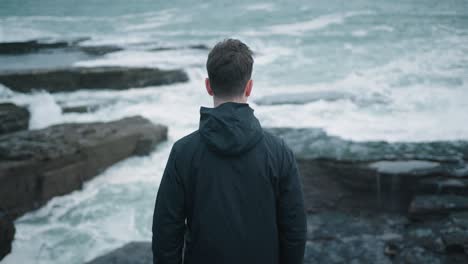 Man-standing-at-the-shoreline-and-looking-into-the-ocean