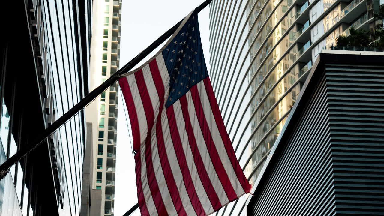 Bandiera americana esposta tra moderni grattacieli, incorniciata da facciate in vetro e architettura urbana, a simboleggiare l'identità nazionale all'interno di un ambiente urbano contemporaneo