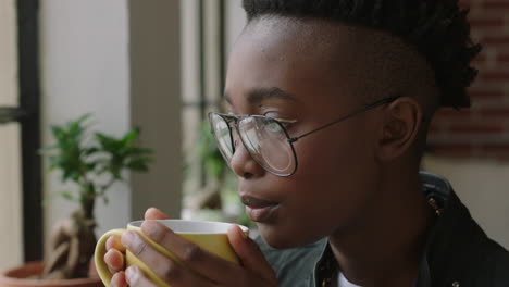 Retrato-Elegante-Joven-Afroamericana-Estudiante-Tomando-Café-En-Casa-Mirando-Por-La-Ventana-Pensando-Planeando-Con-Anticipación-Disfrutando-De-Un-Estilo-De-Vida-Relajante-Usando-Gafas-De-Moda