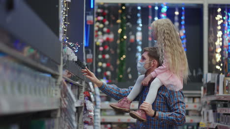 father and daughter on shoulders choose christmas garlands for christmas in the supermarket