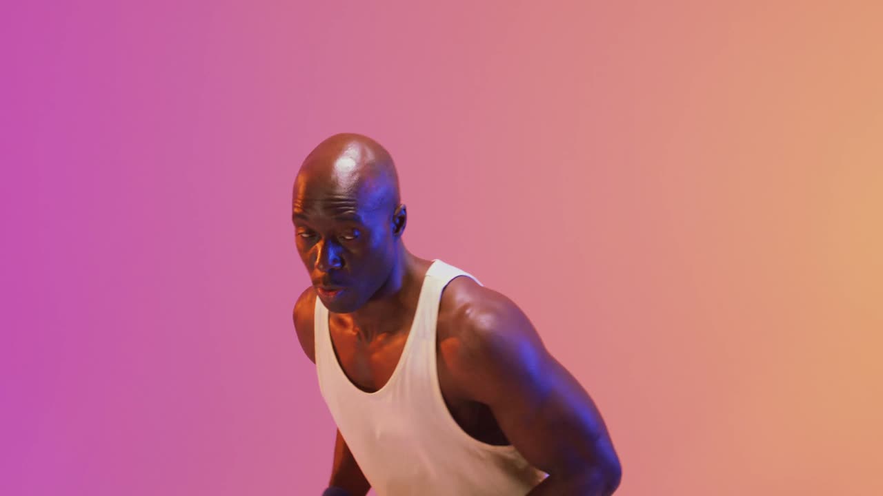 Video af afroamerikansk mandlig basketballspiller, der kaster bolden på en pink til orange baggrund.