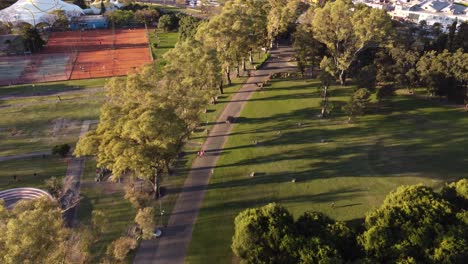 Toma-Aérea-De-La-Conducción-De-Automóviles-En-Park-Path-En-Parque-Sarmiento-Durante-La-Puesta-De-Sol,-Buenos-Aires