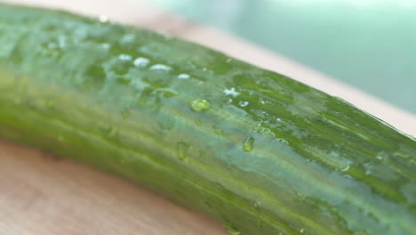 close up pan of a freshly rinsed, whole cucumber resting on a wood cutting board