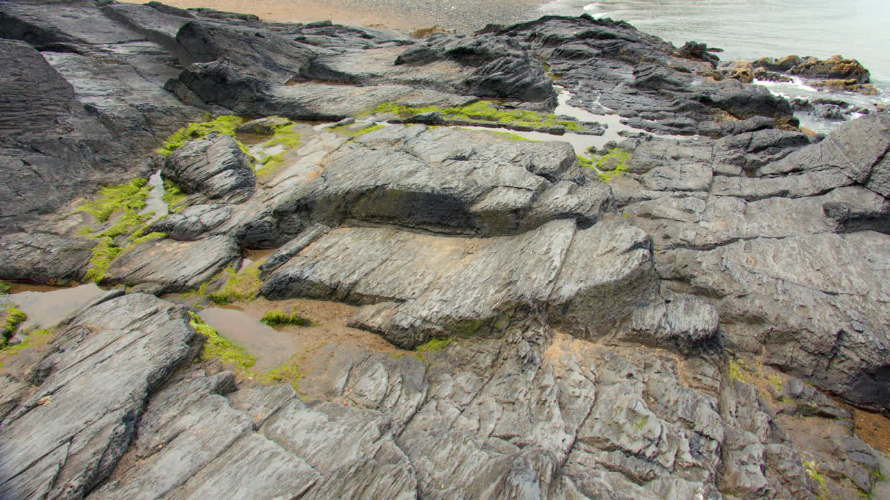 Panning shot right to left of sedimentary rocks at low tide at Tresaith beach