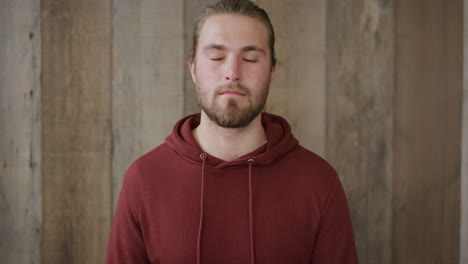 portrait of independent young blonde man looking at camera attractive bearded male wearing hoodie on wooden background slow motion