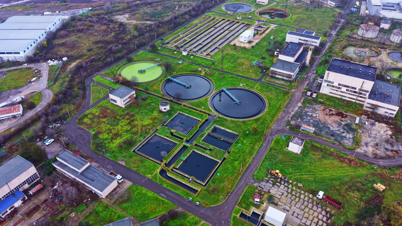 Large water treatment facility located in a city with multiple tanks and structures visible surrounded by green areas and industrial buildings