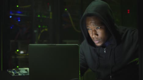 african american male computer hacker using laptop in business server room